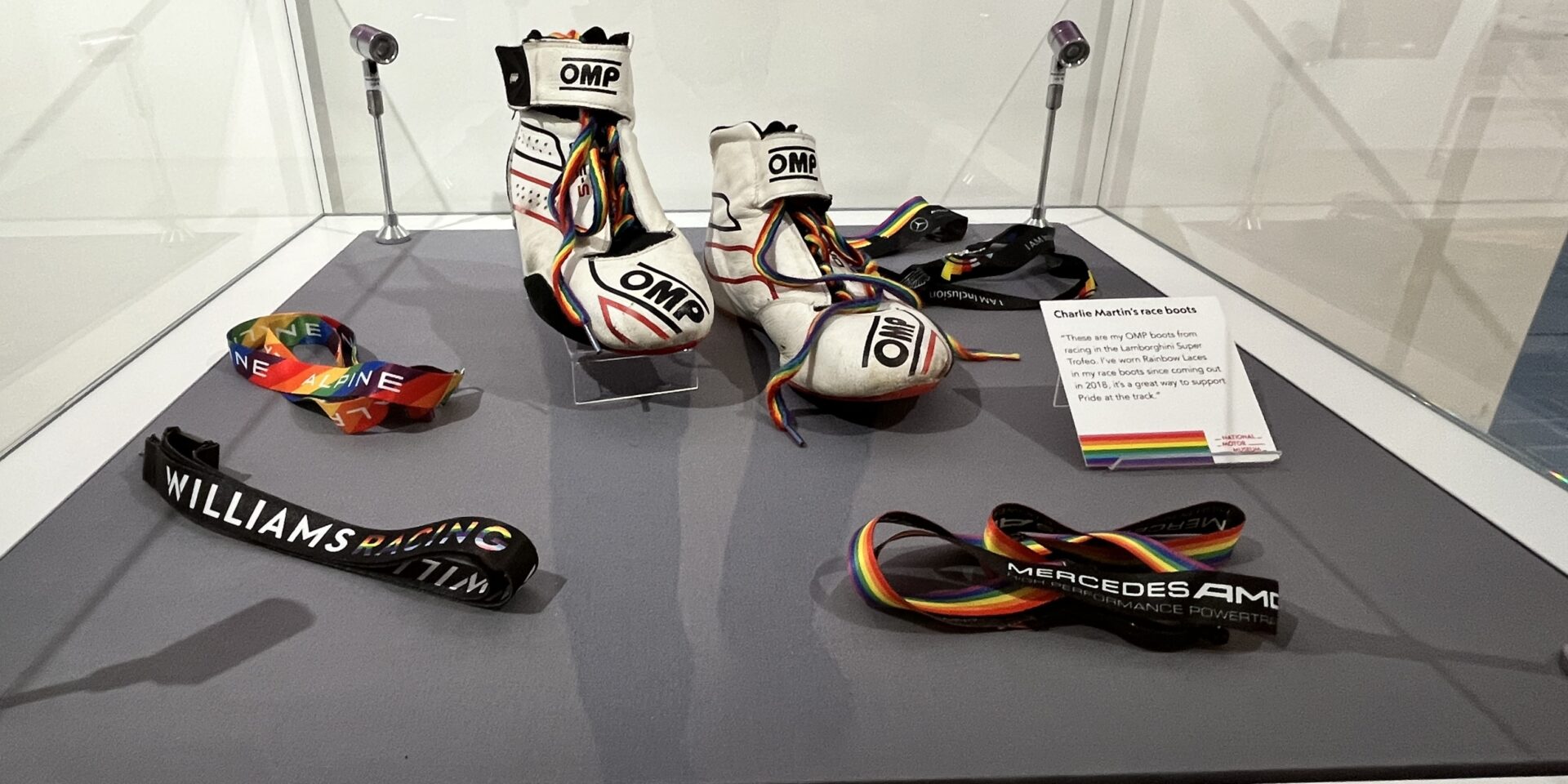 A glass display case including race boots with rainbow laces and various rainbow lanyards.