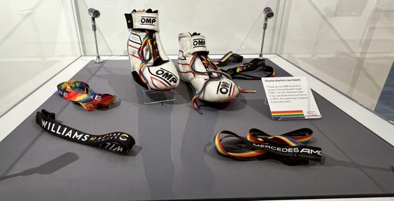 A glass display case including race boots with rainbow laces and various rainbow lanyards.