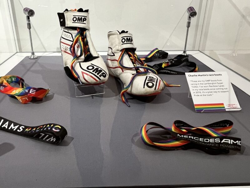 A glass display case including race boots with rainbow laces and various rainbow lanyards.